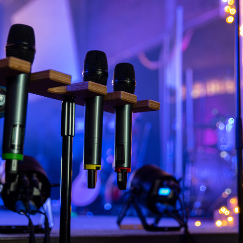 A close-up of microphones with a stage setup in the background.