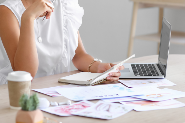 A woman surrounded by paper and an open laptop, preparing to plan events.